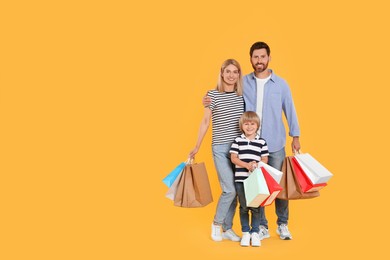 Photo of Family shopping. Happy parents and son with paper bags on orange background. Space for text