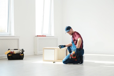 Photo of Handyman in uniform assembling furniture indoors. Professional construction tools