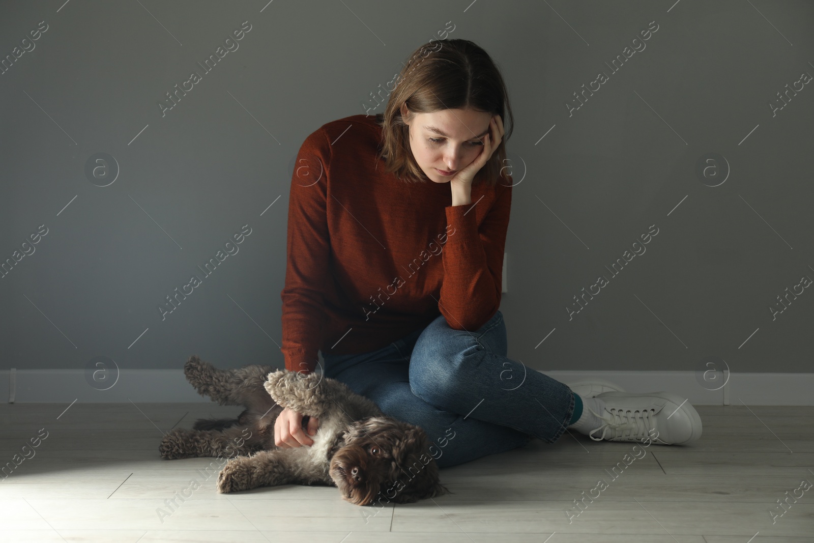 Photo of Sad young woman sitting on floor near grey wall indoors