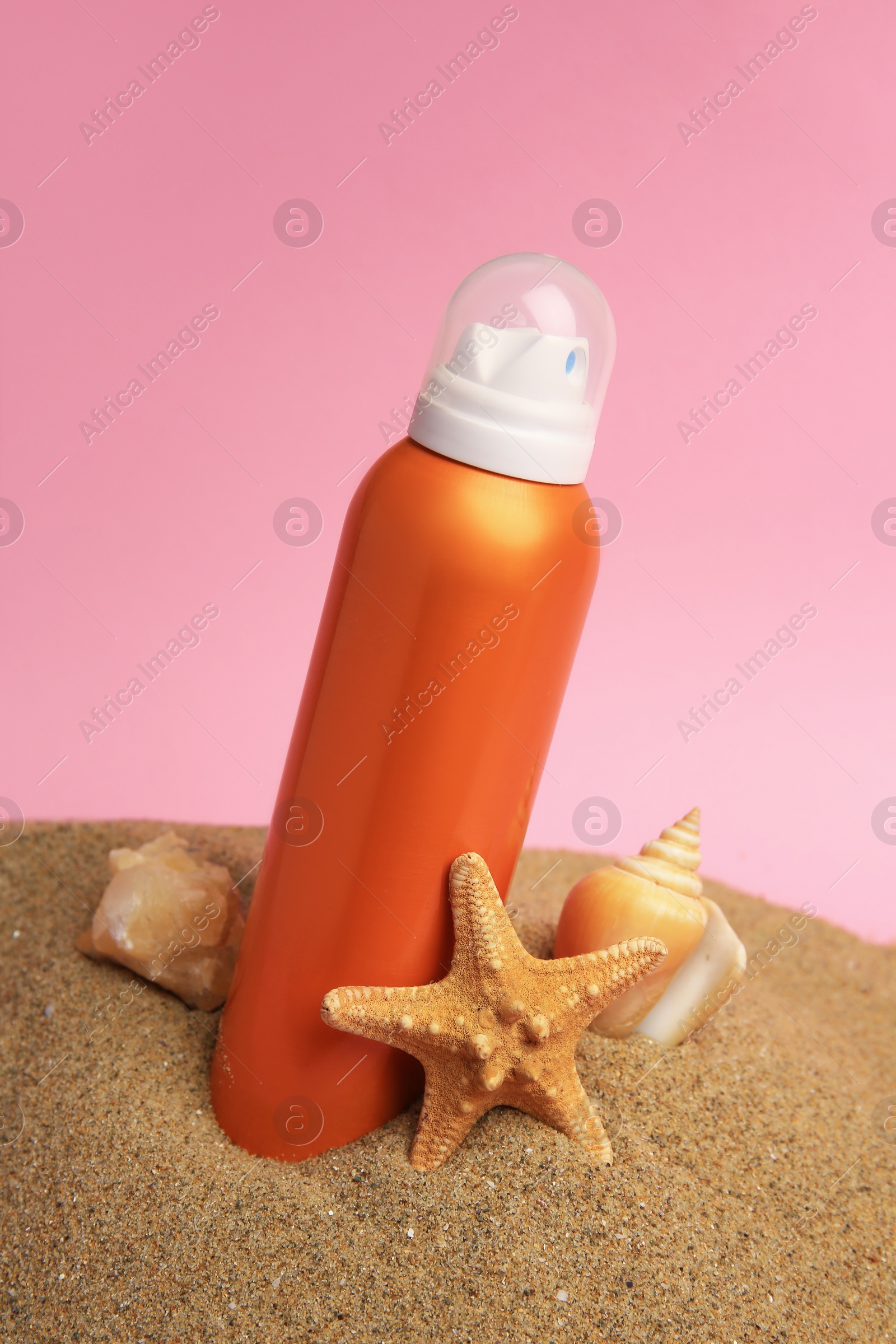 Photo of Sand with sunscreen, stone, starfish and seashell against pink background. Sun protection care
