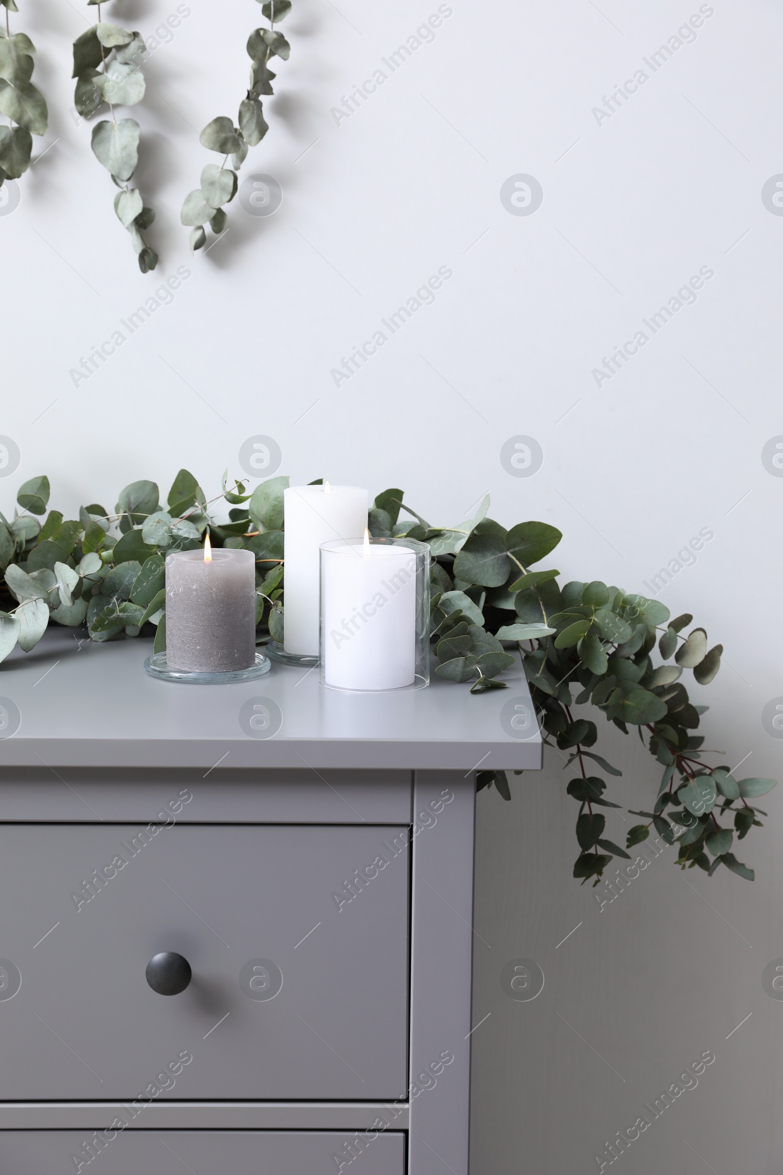 Photo of Stylish chest of drawers decorated with beautiful eucalyptus garland and candles indoors