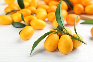 Photo of Fresh ripe kumquats with green leaves on white wooden table