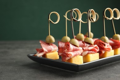 Tasty canapes with olives, prosciutto and cheese on grey table, closeup. Space for text