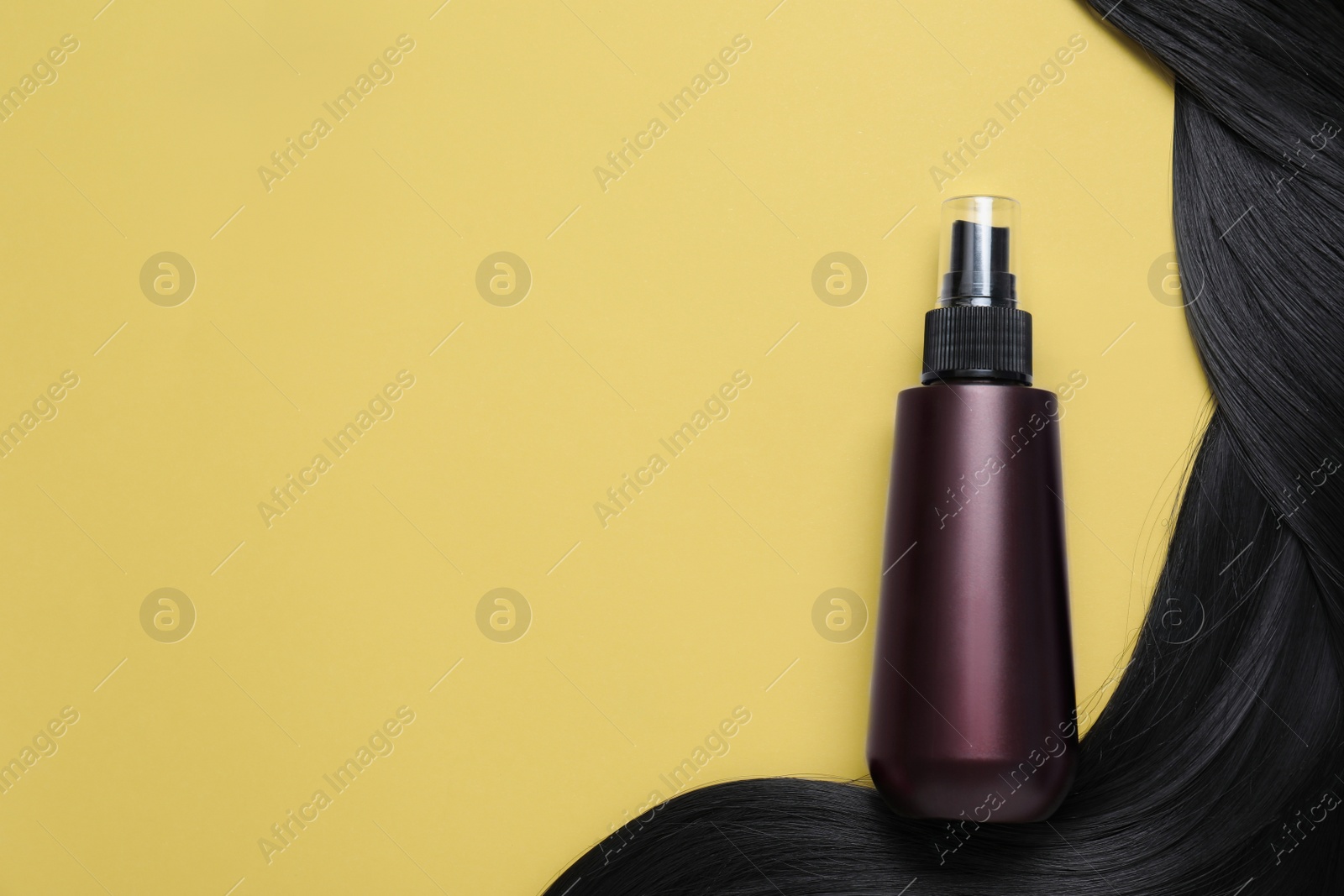 Photo of Spray bottle with thermal protection and lock of black hair on yellow background, flat lay. Space for text