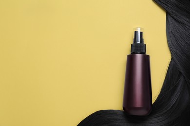 Photo of Spray bottle with thermal protection and lockblack hair on yellow background, flat lay. Space for text
