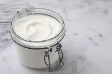 Photo of Delicious natural yogurt in glass jar on white marble table, closeup. Space for text