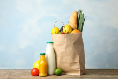 Paper bag with groceries on wooden table against light blue background