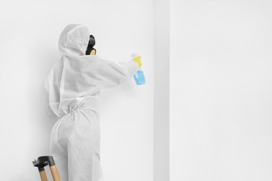 Photo of Woman in protective suit cleaning mold with sprayer on wall indoors. Space for text