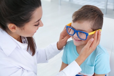 Children's doctor putting glasses on little boy in clinic