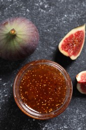 Photo of Jar with tasty sweet jam and fresh figs on black textured table, flat lay