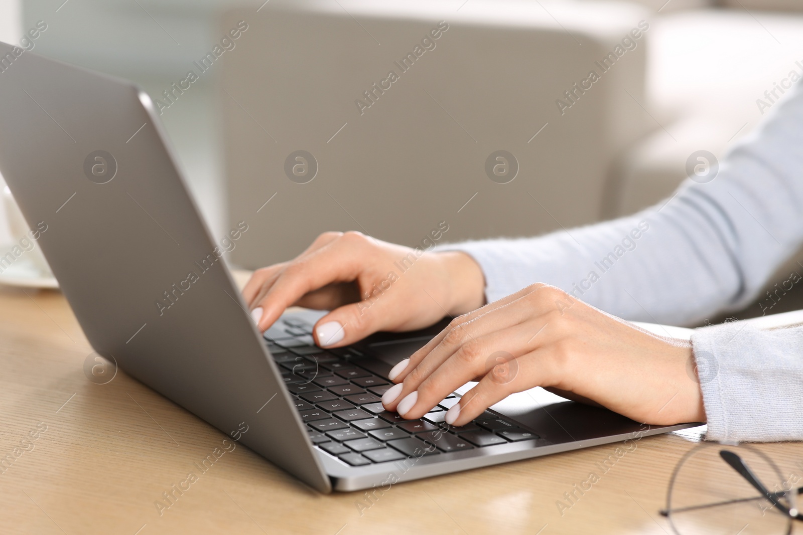 Photo of Woman working with laptop at wooden desk indoors, closeup