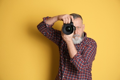 Mature male photographer with camera on color background