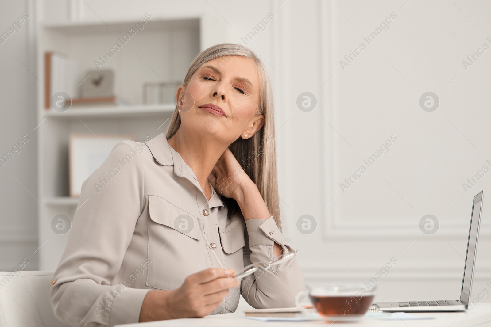 Photo of Woman suffering from neck pain at workplace in room