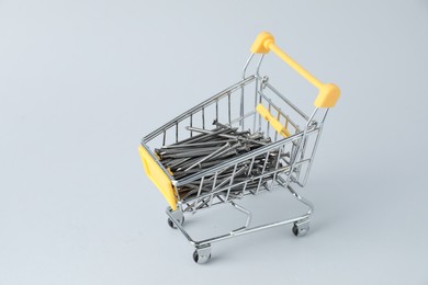 Photo of Metal nails in shopping cart on light grey background