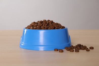 Dry food in light blue pet bowl on wooden surface