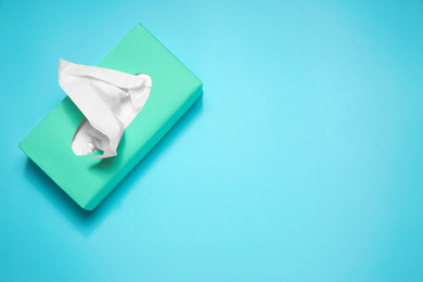 Photo of Box with paper tissues on light blue background, top view. Space for text