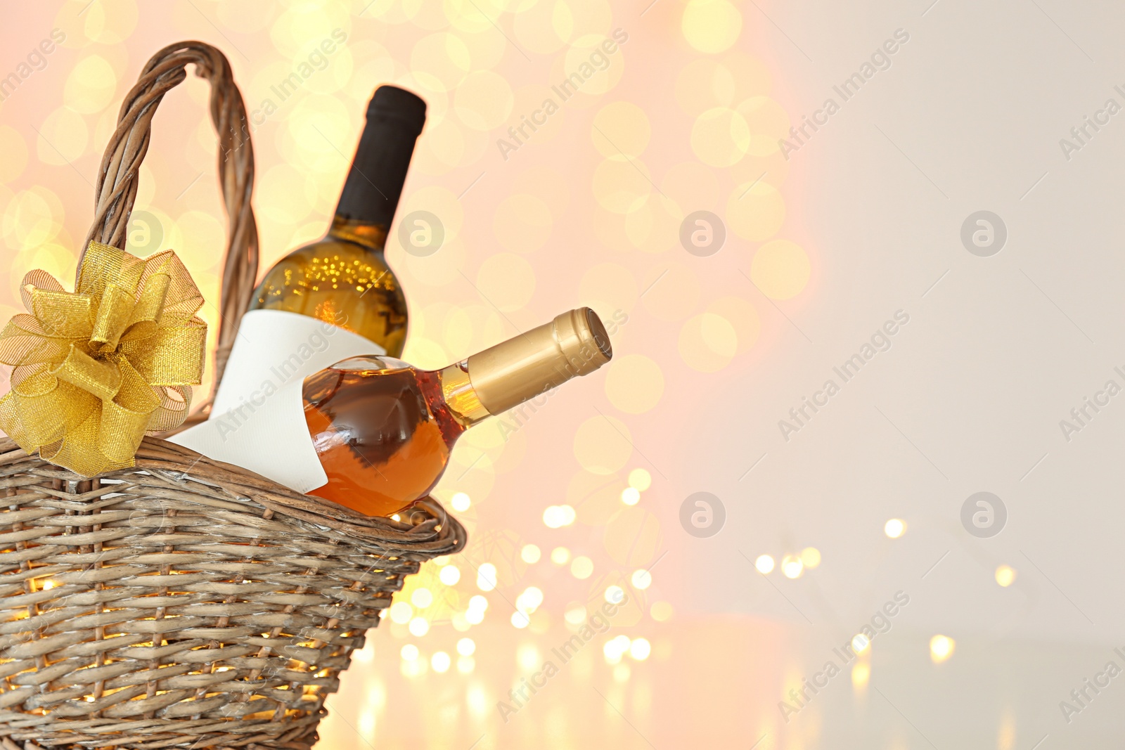 Photo of Wicker basket with bottles of wine against blurred lights. Space for text