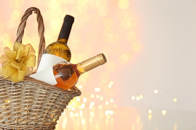 Photo of Wicker basket with bottles of wine against blurred lights. Space for text