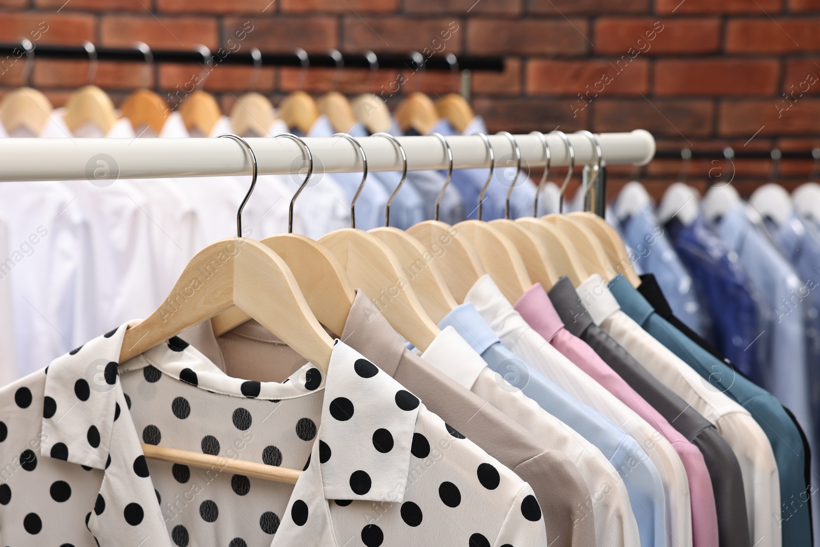 Photo of Dry-cleaning service. Many different clothes hanging on rack against brick wall, closeup