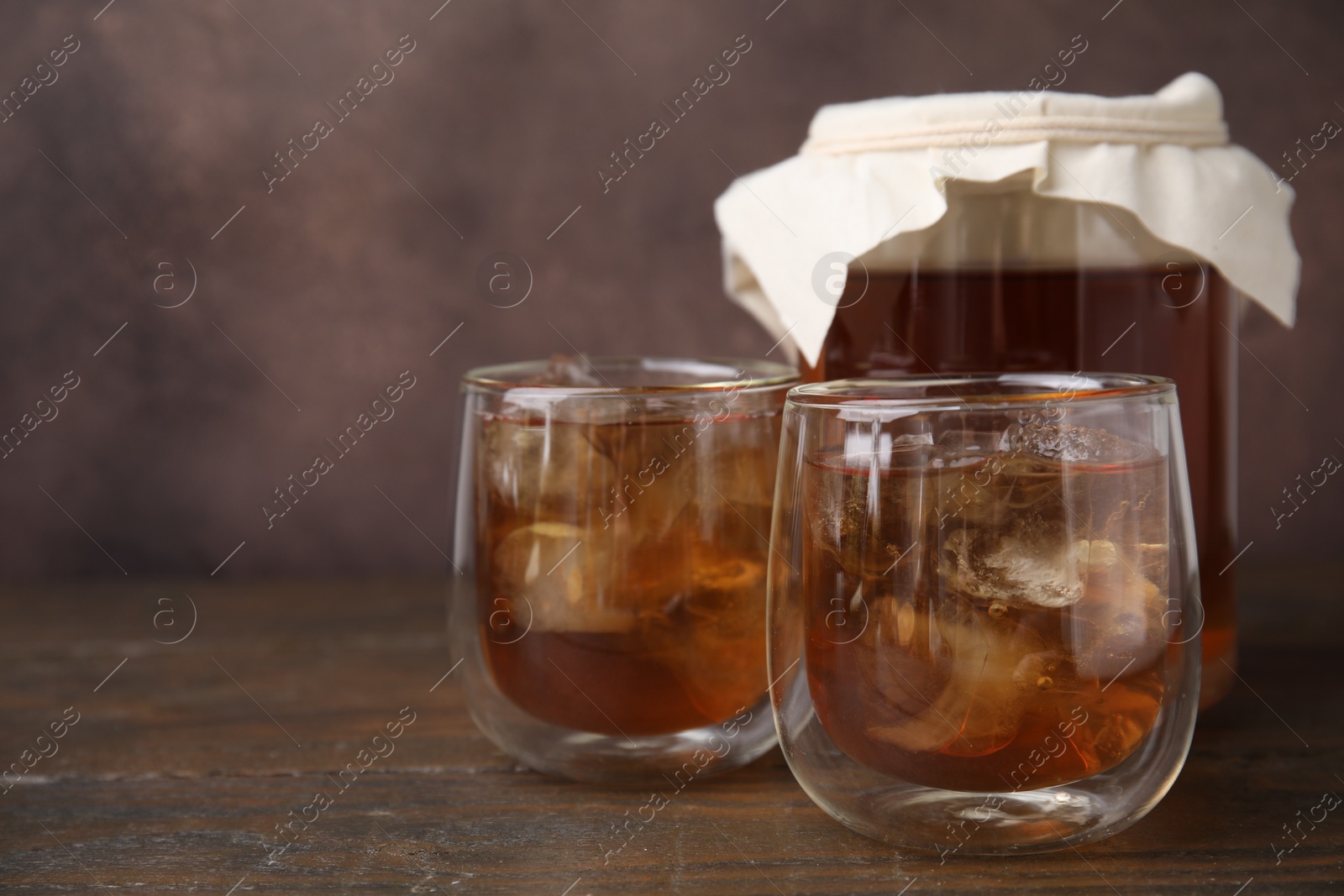Photo of Tasty kombucha with ice cubes on wooden table, closeup. Space for text