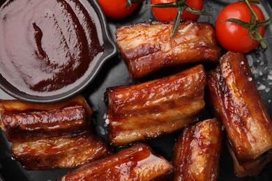 Photo of Tasty roasted pork ribs with sauce and tomatoes on plate, flat lay