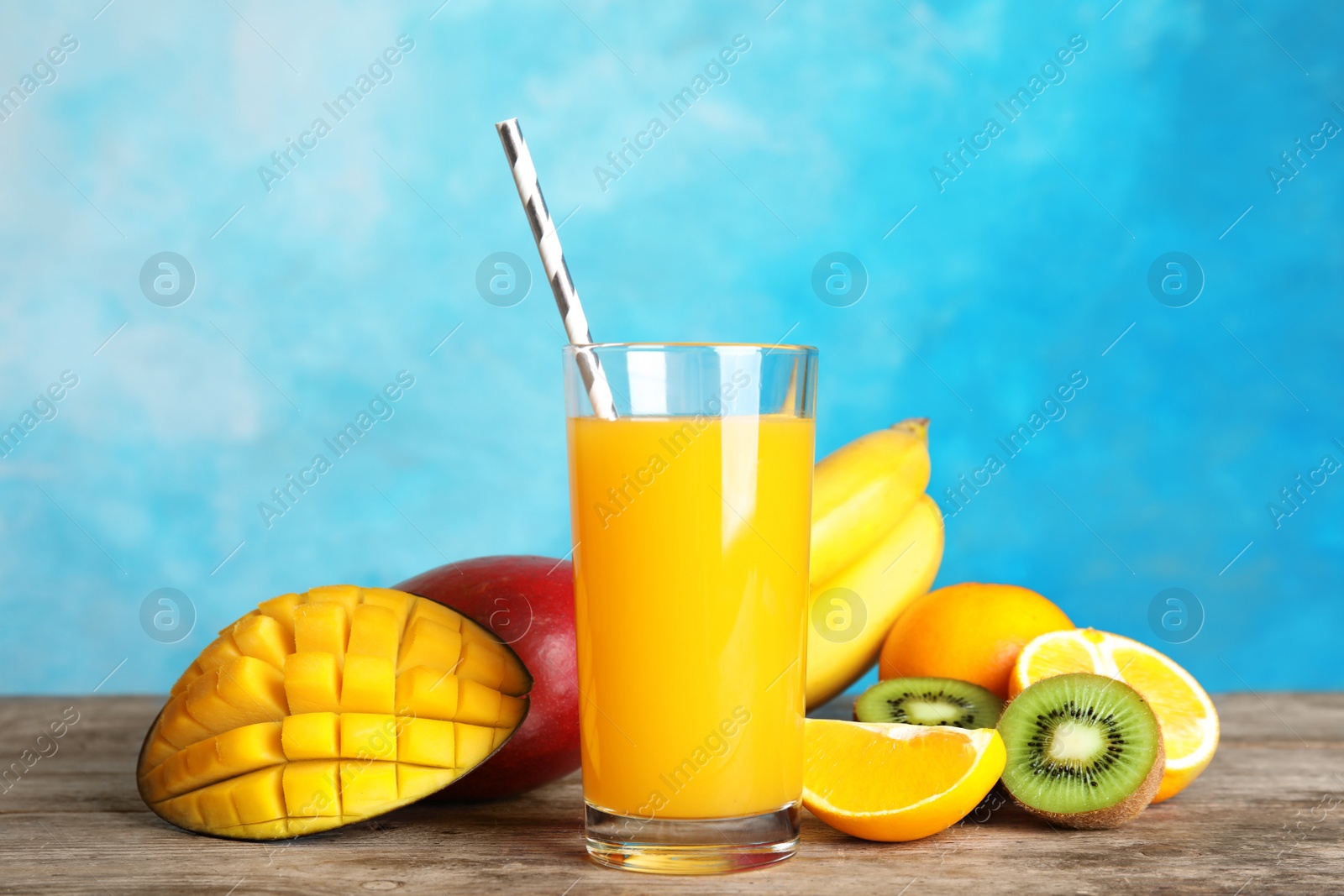 Photo of Glass with tasty mango juice and fresh fruits on table against color background