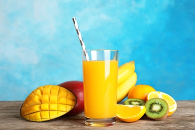 Photo of Glass with tasty mango juice and fresh fruits on table against color background