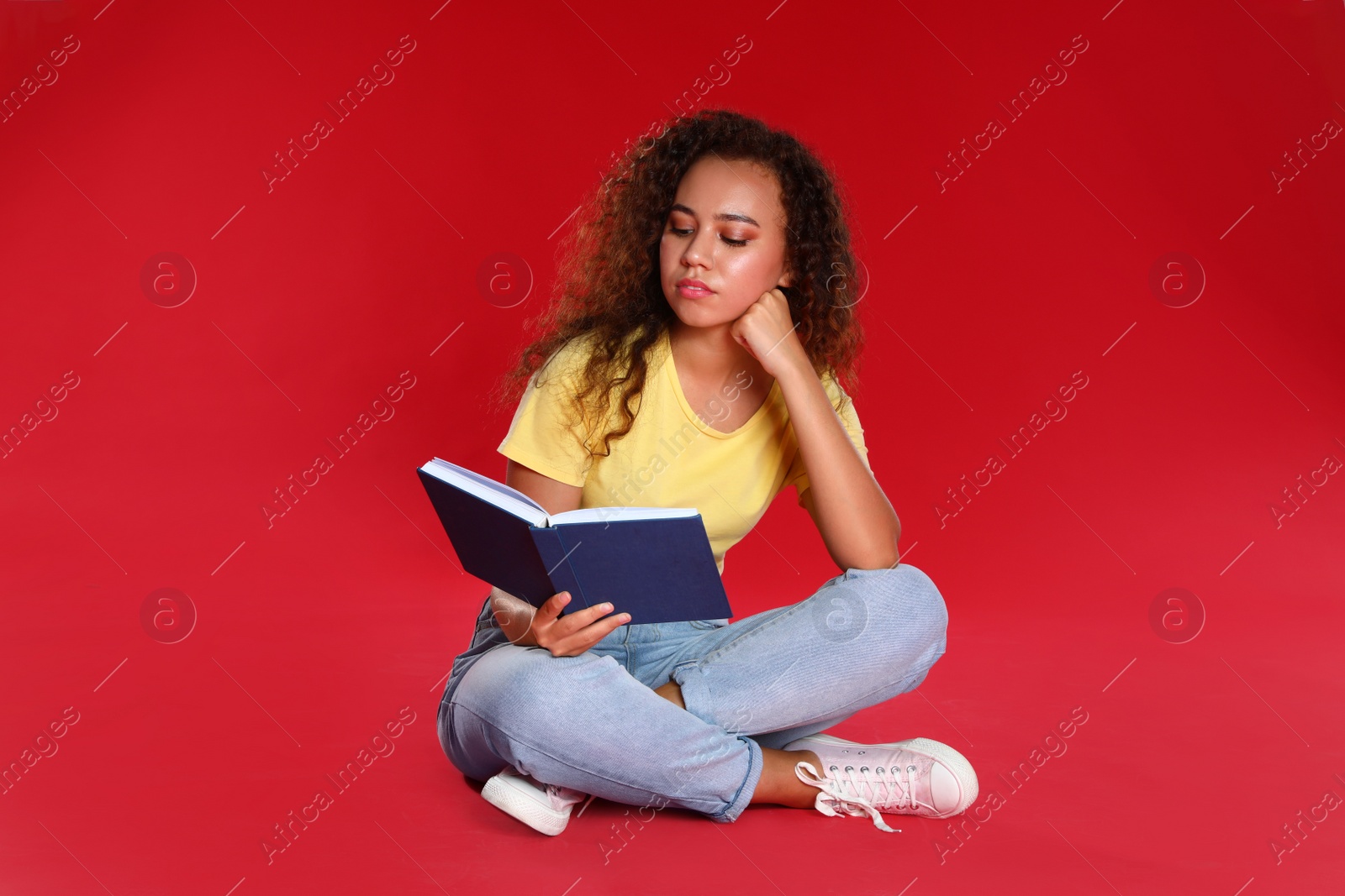 Photo of Beautiful African-American young woman reading book on red background