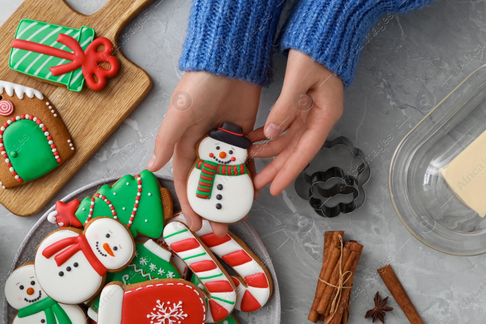 Photo of Woman holding delicious homemade Christmas cookie at grey marble table, top view