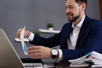 Photo of Businessman working with laptop and documents at table in office