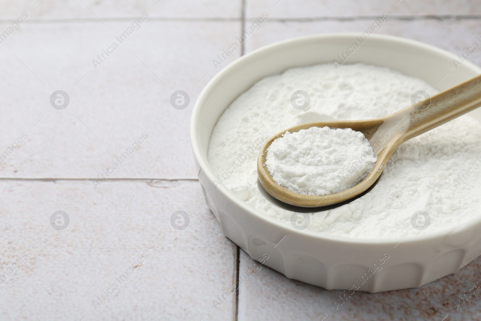 Photo of Baking powder in bowl and spoon on light tiled table, closeup. Space for text