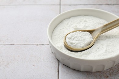 Photo of Baking powder in bowl and spoon on light tiled table, closeup. Space for text