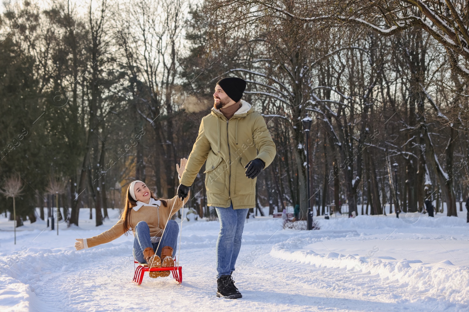 Photo of Happy young man pulling his girlfriend in sleigh outdoors on winter day