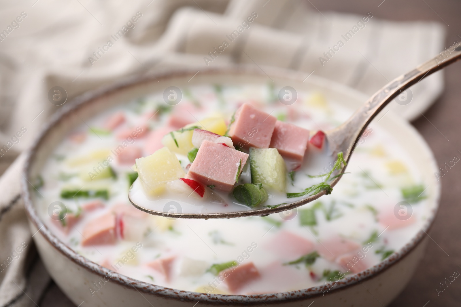 Photo of Eating delicious cold summer soup (okroshka) with boiled sausage at table, closeup