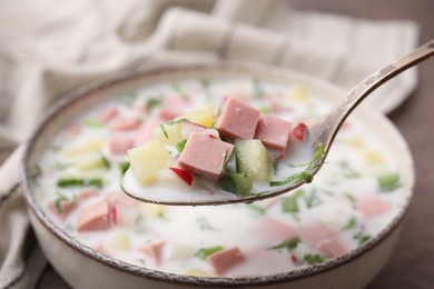 Eating delicious cold summer soup (okroshka) with boiled sausage at table, closeup