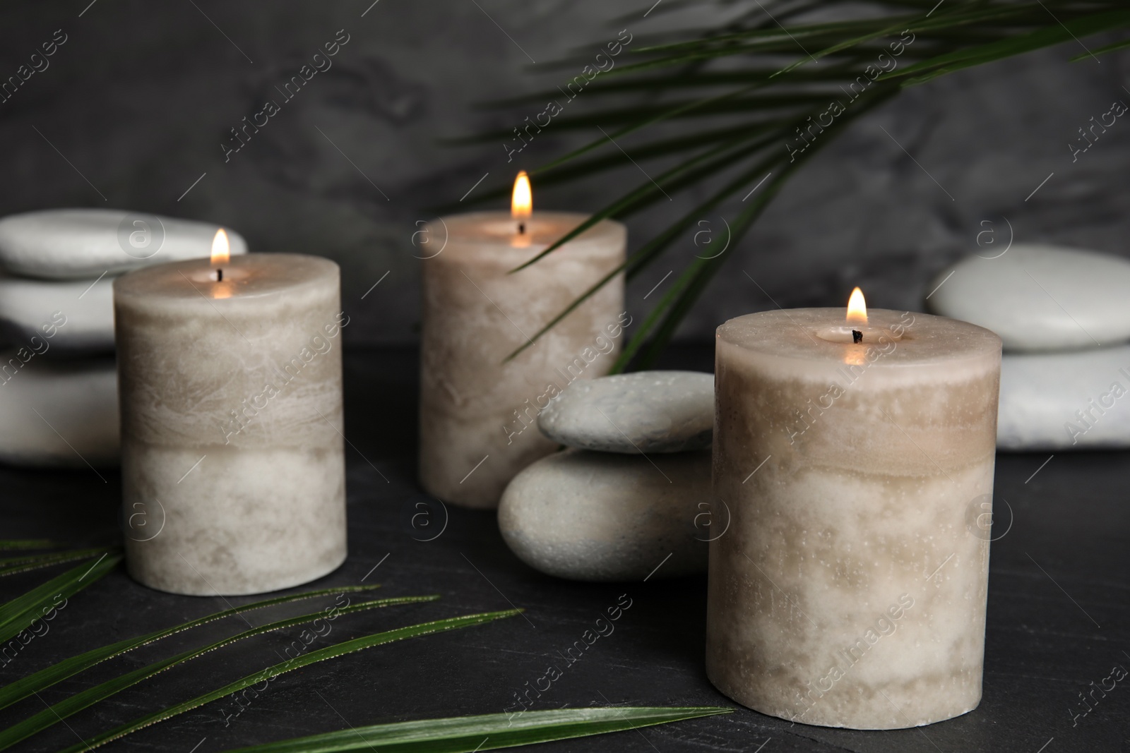 Photo of Burning candles and spa stones on dark table