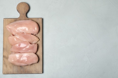 Wooden board with raw chicken meat on gray background, top view. Space for text