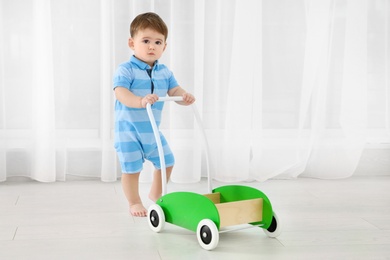 Cute baby playing with toy walker, indoors