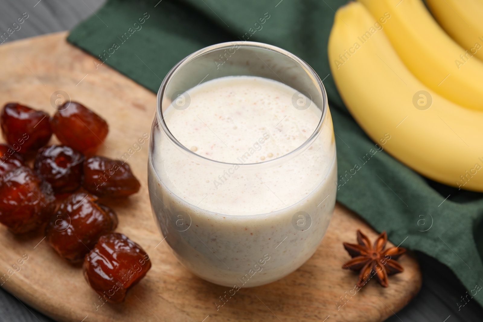 Photo of Glass of delicious date smoothie, dried fruits and anise on wooden board, closeup