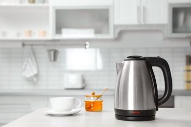 Photo of Modern electric kettle, cup and honey on wooden table in kitchen