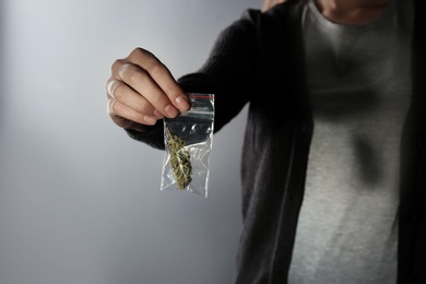 Photo of Female dealer holding hemp in plastic bag on color background, closeup