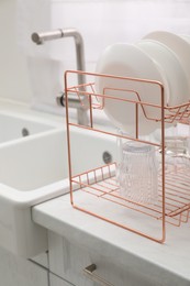 Drying rack with clean dishes on light marble countertop near sink in kitchen