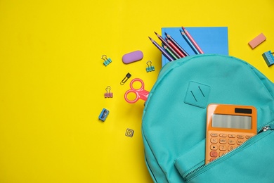 Stylish backpack with different school stationary on yellow background, top view. Space for text