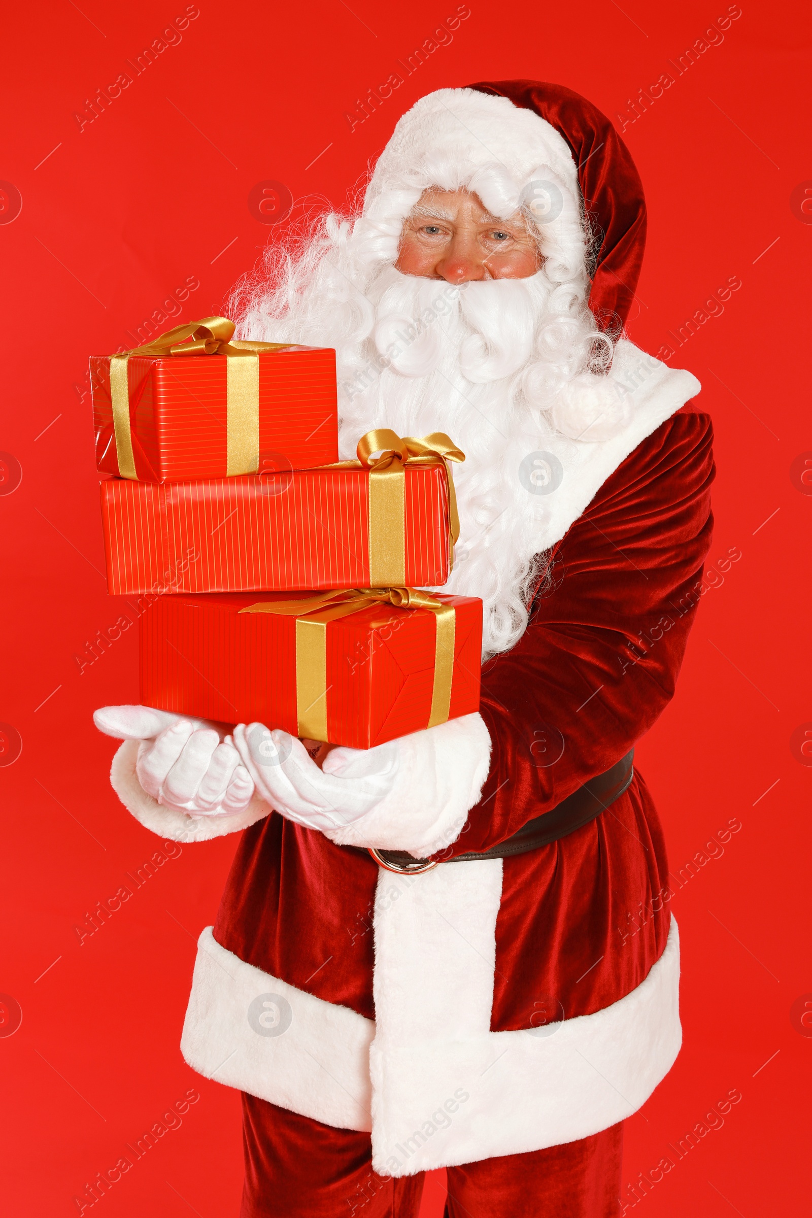 Photo of Authentic Santa Claus with gift boxes on red background