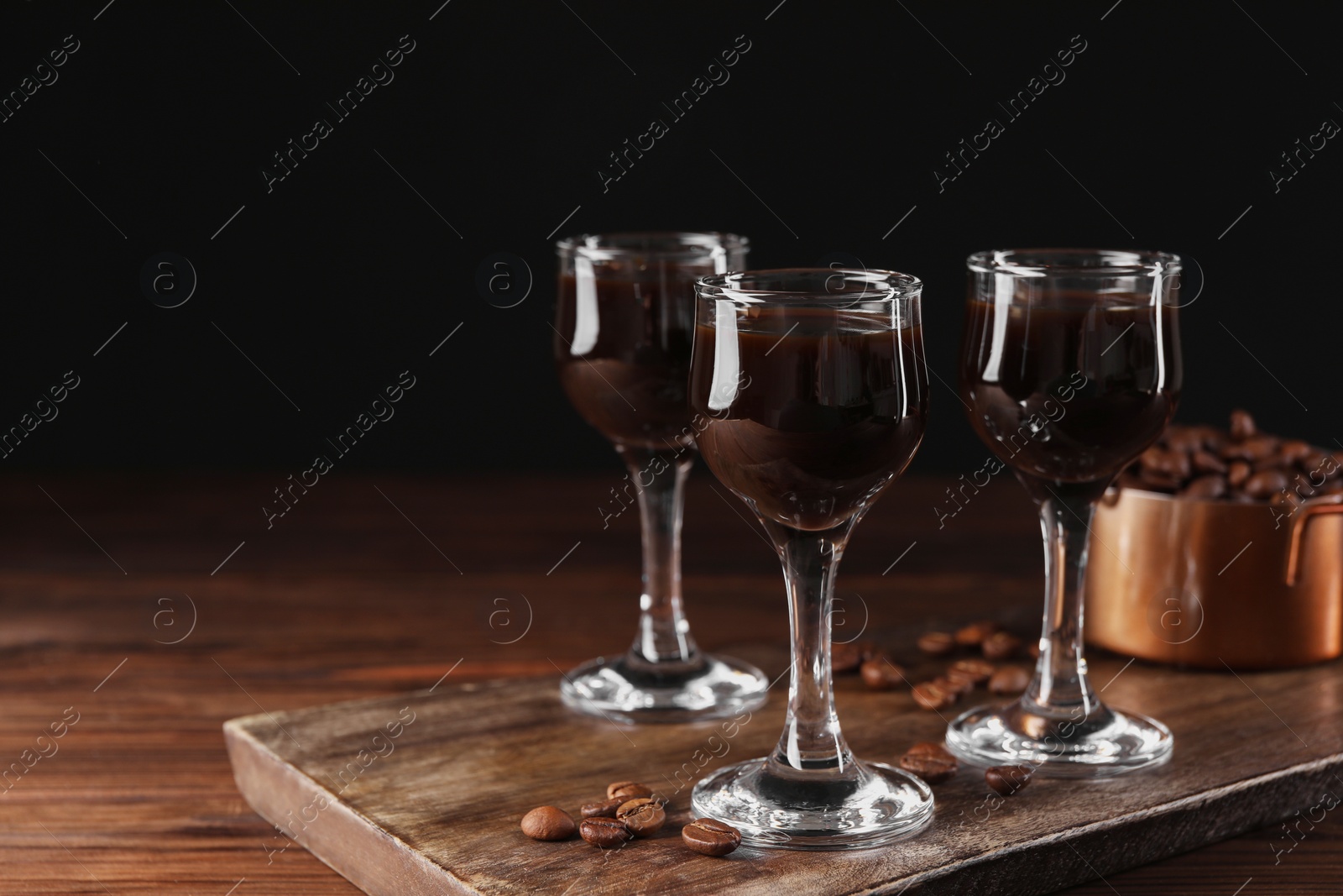 Photo of Shot glasses with coffee liqueur and beans on wooden table, space for text