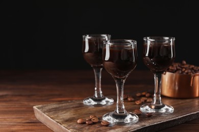 Photo of Shot glasses with coffee liqueur and beans on wooden table, space for text