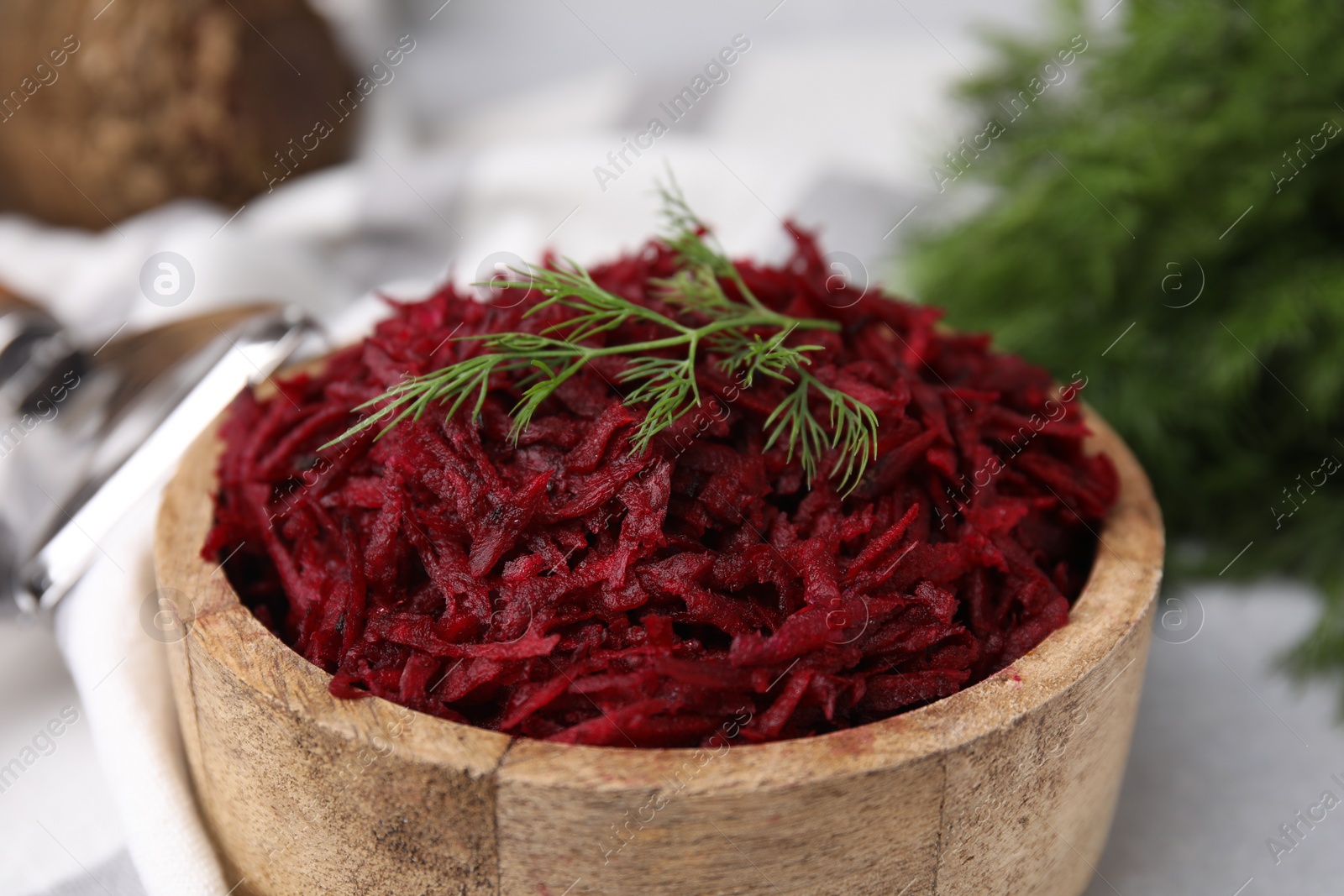 Photo of Grated red beet and dill in wooden bowl on table, closeup