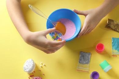 Little girl making slime toy on yellow background, top view