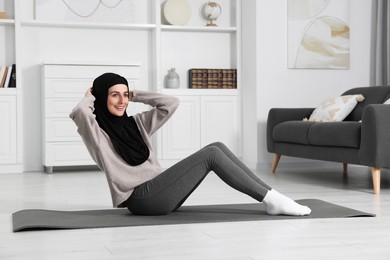 Photo of Muslim woman in hijab doing abs exercise on fitness mat at home