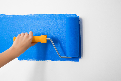 Photo of Woman painting white wall with blue dye, closeup. Interior renovation
